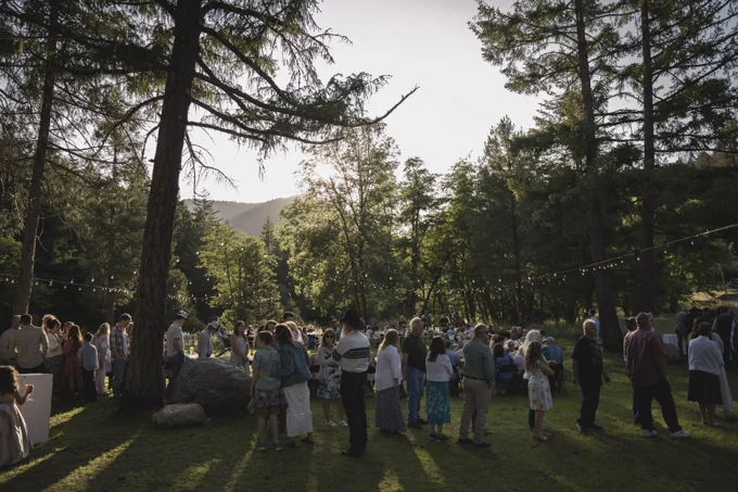 Guests gathering outdoors beneath tall trees and string lights