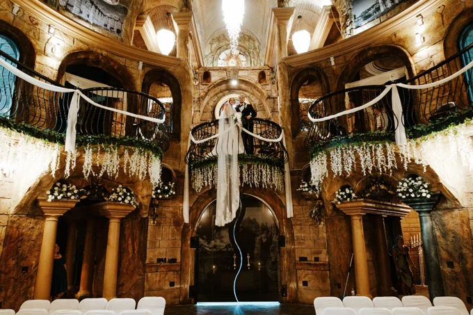 Newlyweds on the chapel balcony surrounded by stone arches and floral draping