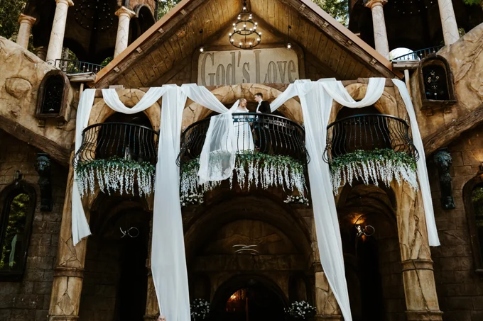 Chapel facade decorated with white draping and flowers, with a couple on the balcony