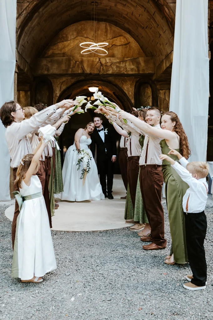 Wedding party holding flowers above newlyweds outside the chapel