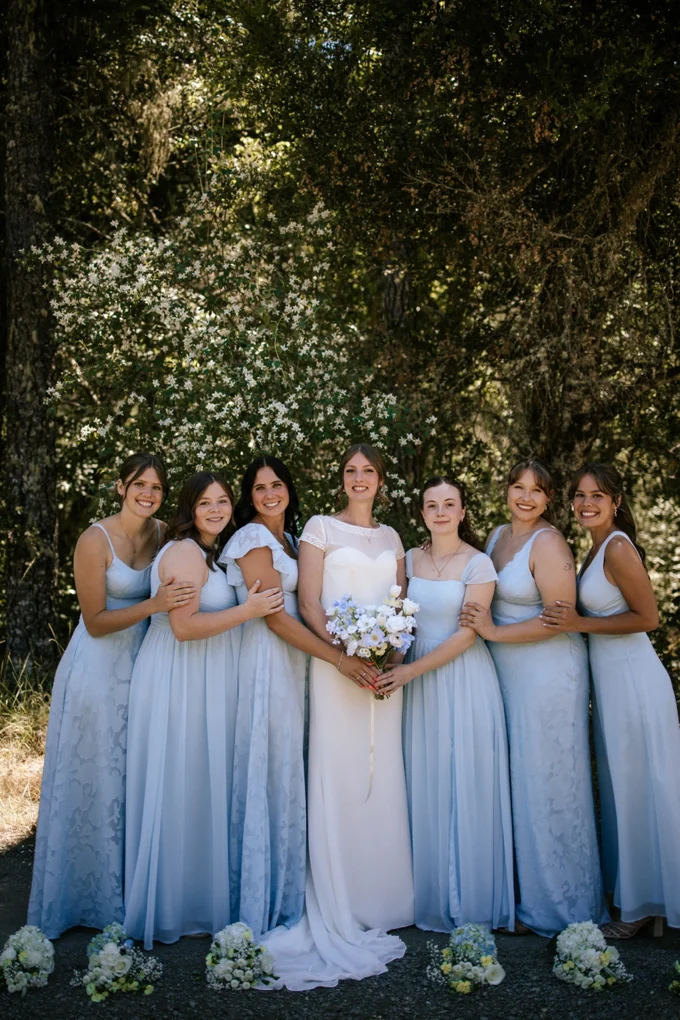Bride and wedding party posing with bouquets beneath the trees
